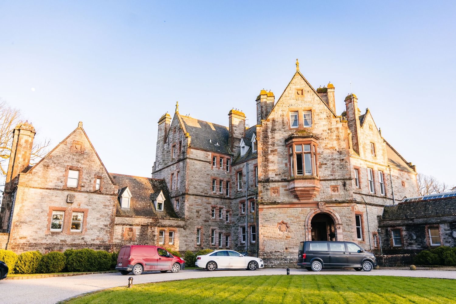 Castle Leslie Wedding Photographer DubGothic stone mansion with turrets and spires against a sunset sky with parked cars in the foreground.