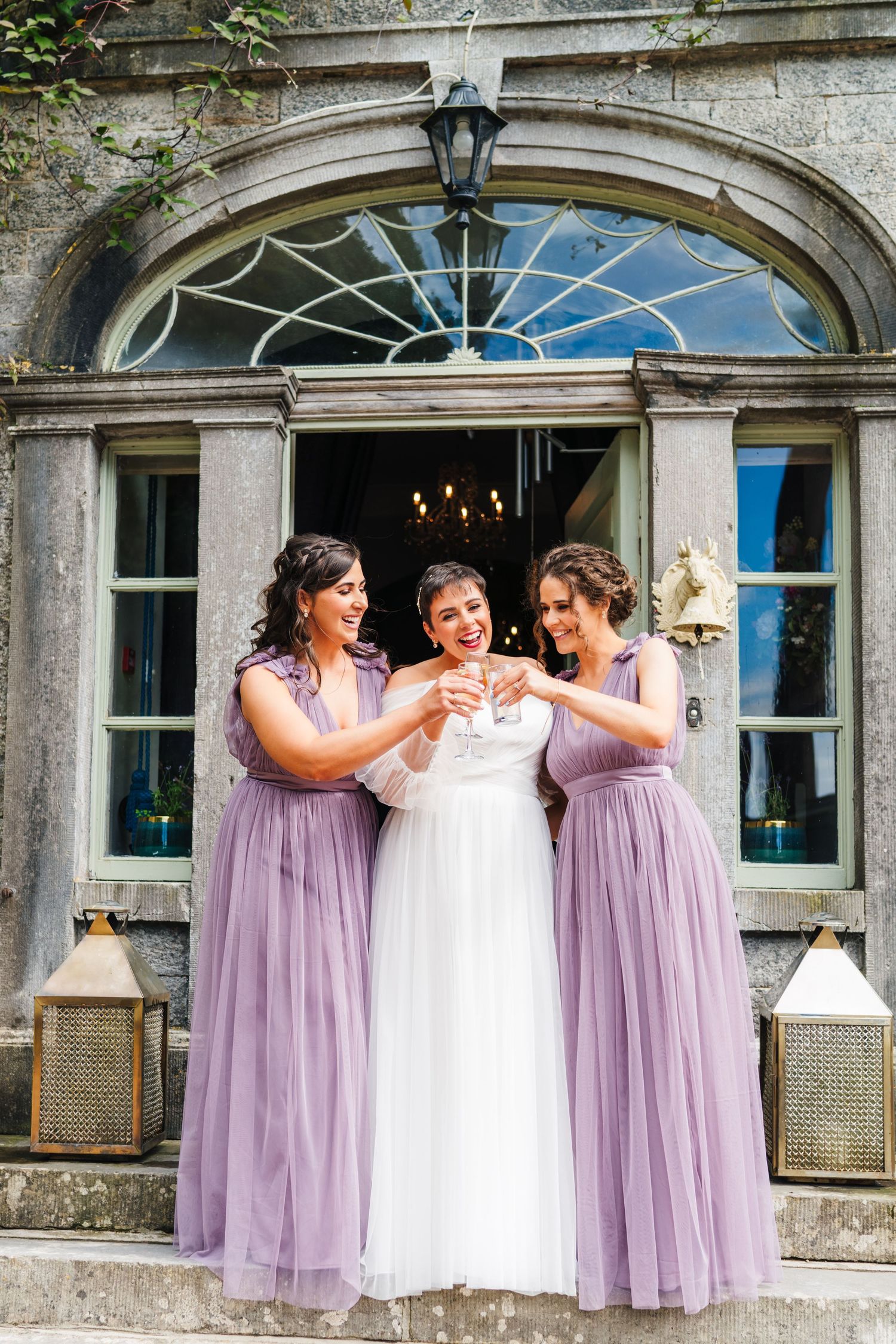 Millhouse slane wedding photographer dublin Bridesmaids in lavender dresses help adjust wedding gown in front of elegant arched doorway.