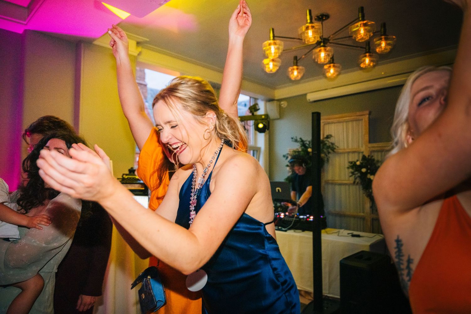 Wedding guest in navy blue dress dances energetically at reception under pink lighting. PHOTOGRAPHER Dublin Ireland Wedding