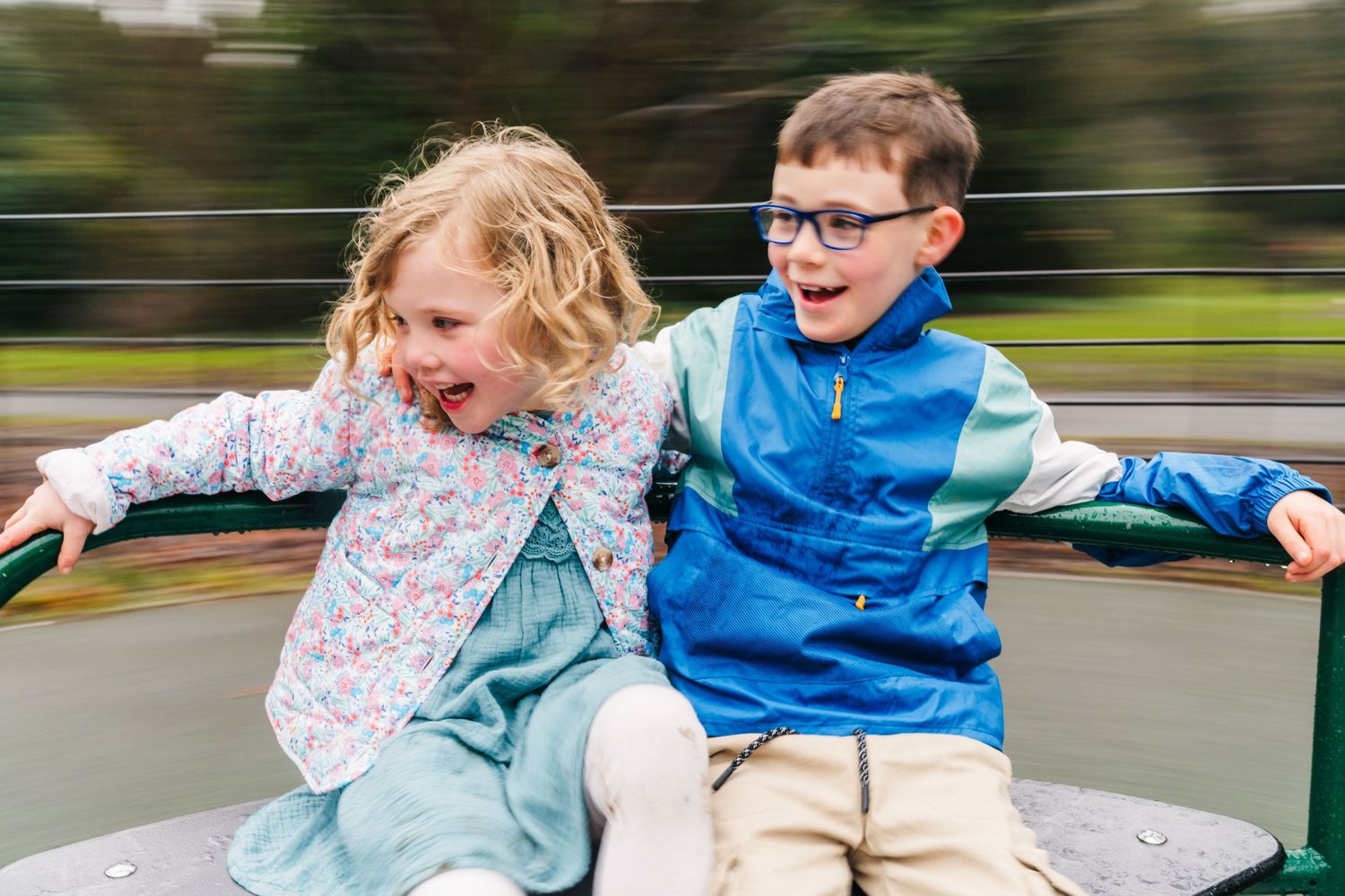 Family photographer Dublin Ireland  Two excited children enjoy spinning on playground equipment with motion blur in background.