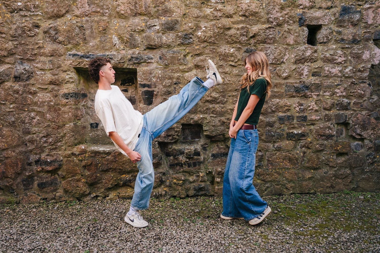 Two people in denim playfully interact against an old stone wall while one performs a dramatic high kick motion. Photographer Ireland dublin