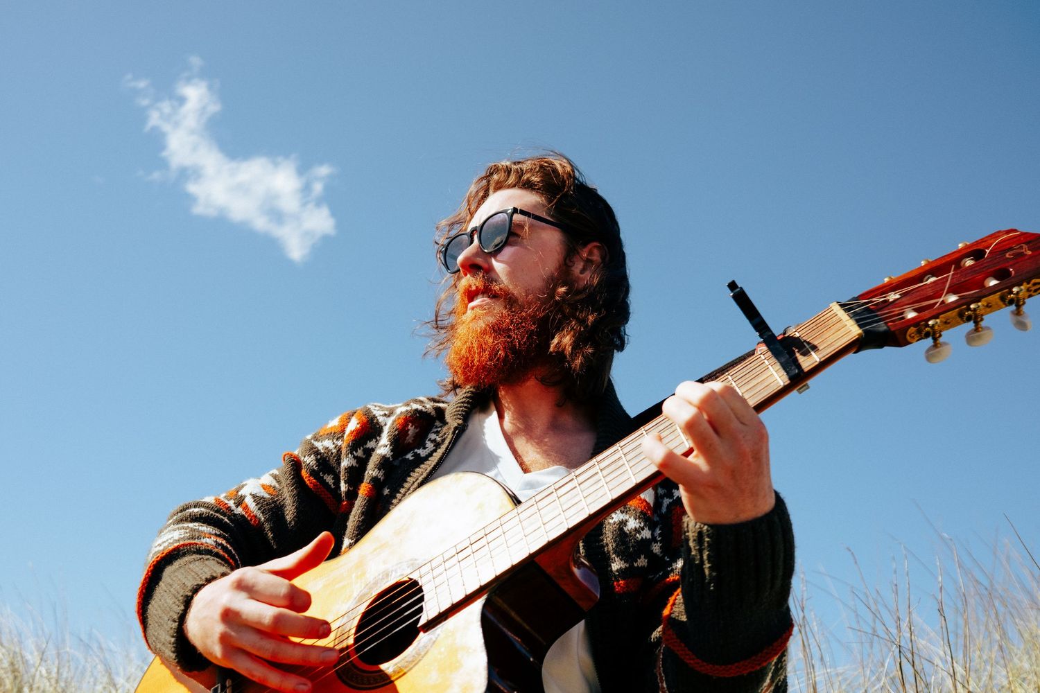 Close-up shot of hands strumming acoustic guitar strings in natural outdoor setting. PHOTOGRAPHER Dublin