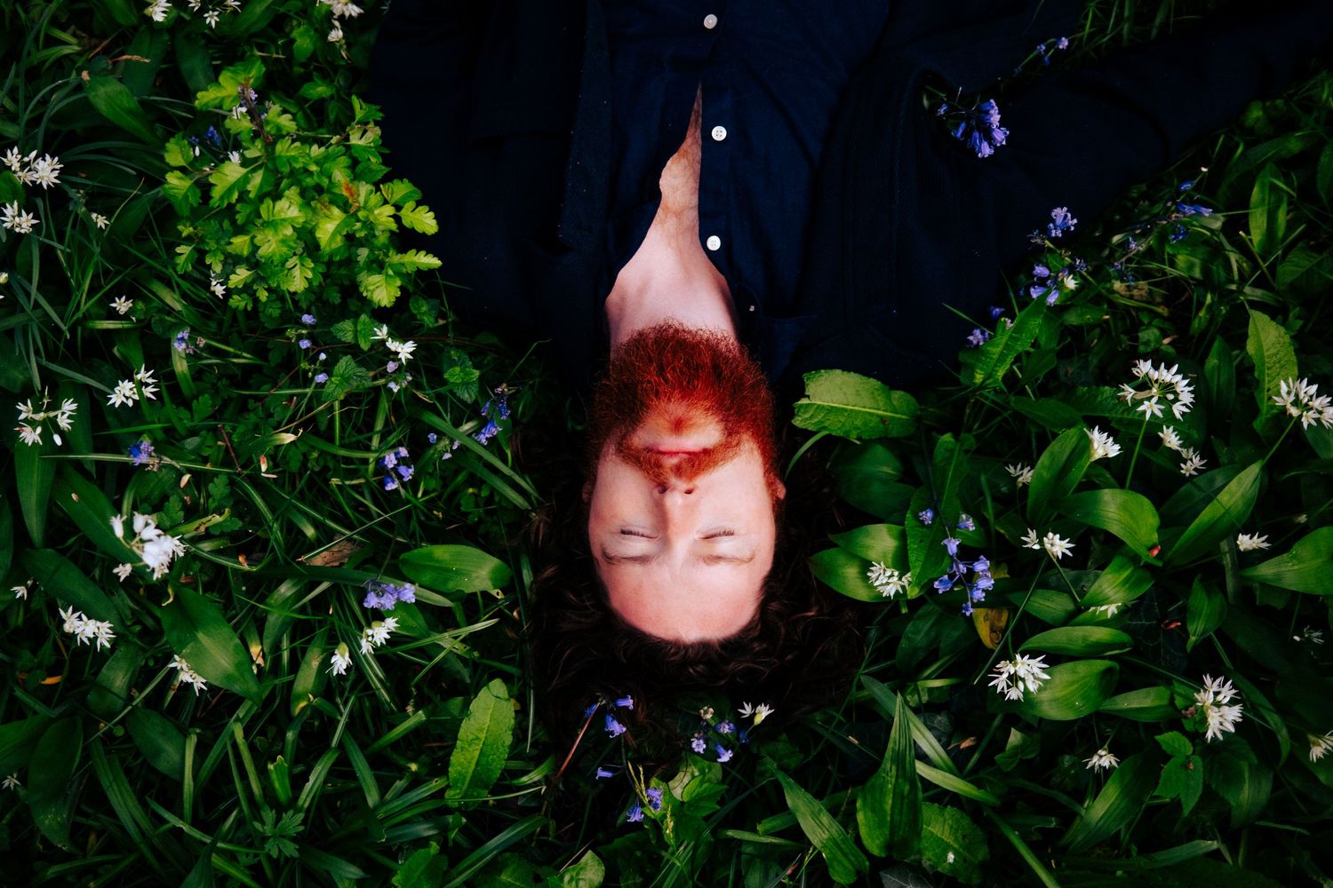 Close up of someone lying in green foliage with small white flowers. PHOTOGRAPHER Dublin