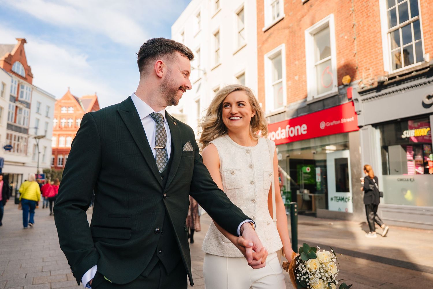 Couple walking hand in hand along a vibrant orange-walled street with shops. City Hall Dublin wedding photogrAPher