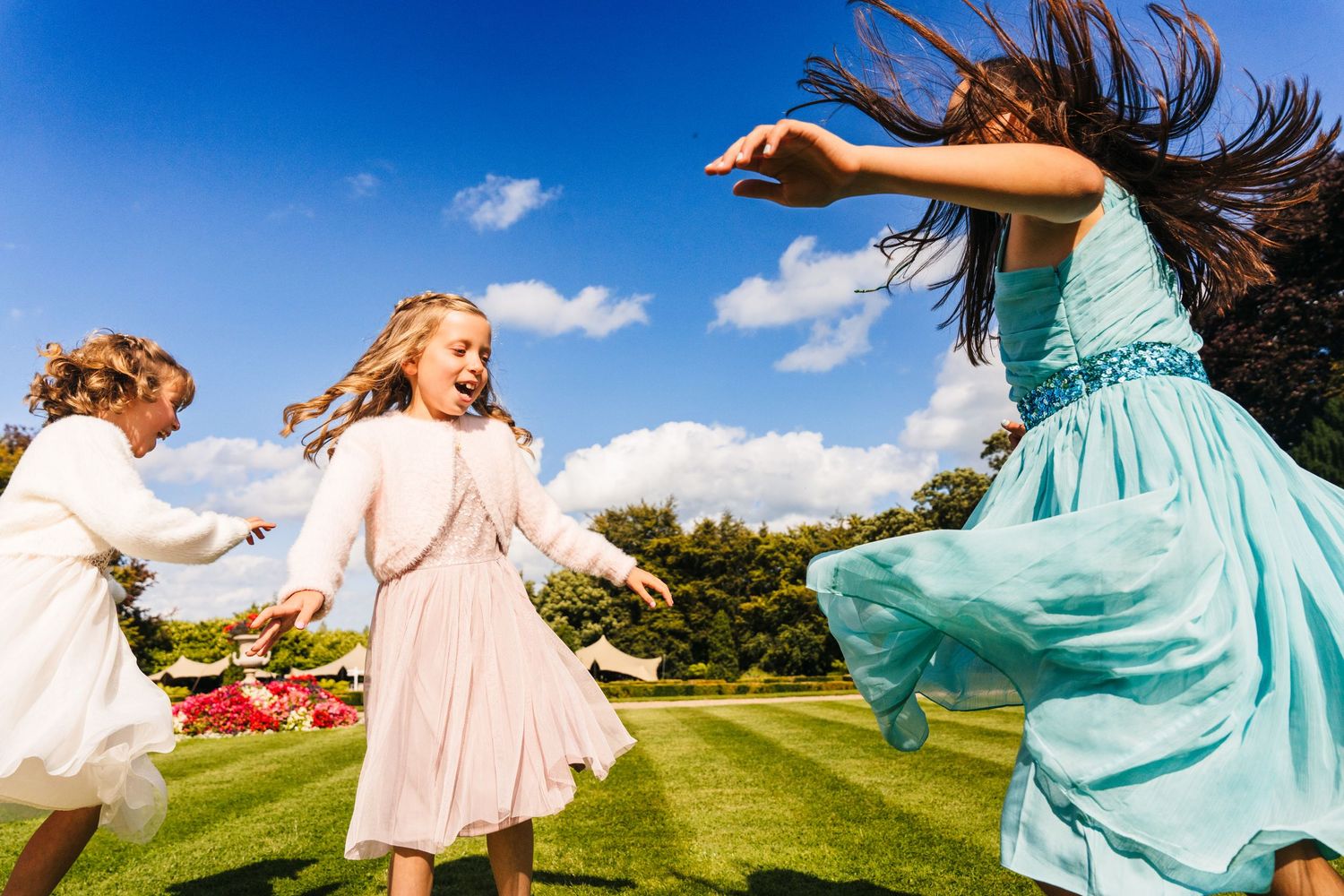 Bridesmaids in turquoise and blush dresses twirl and dance together on a sunny green hillside. Wedding Photographer Dublin