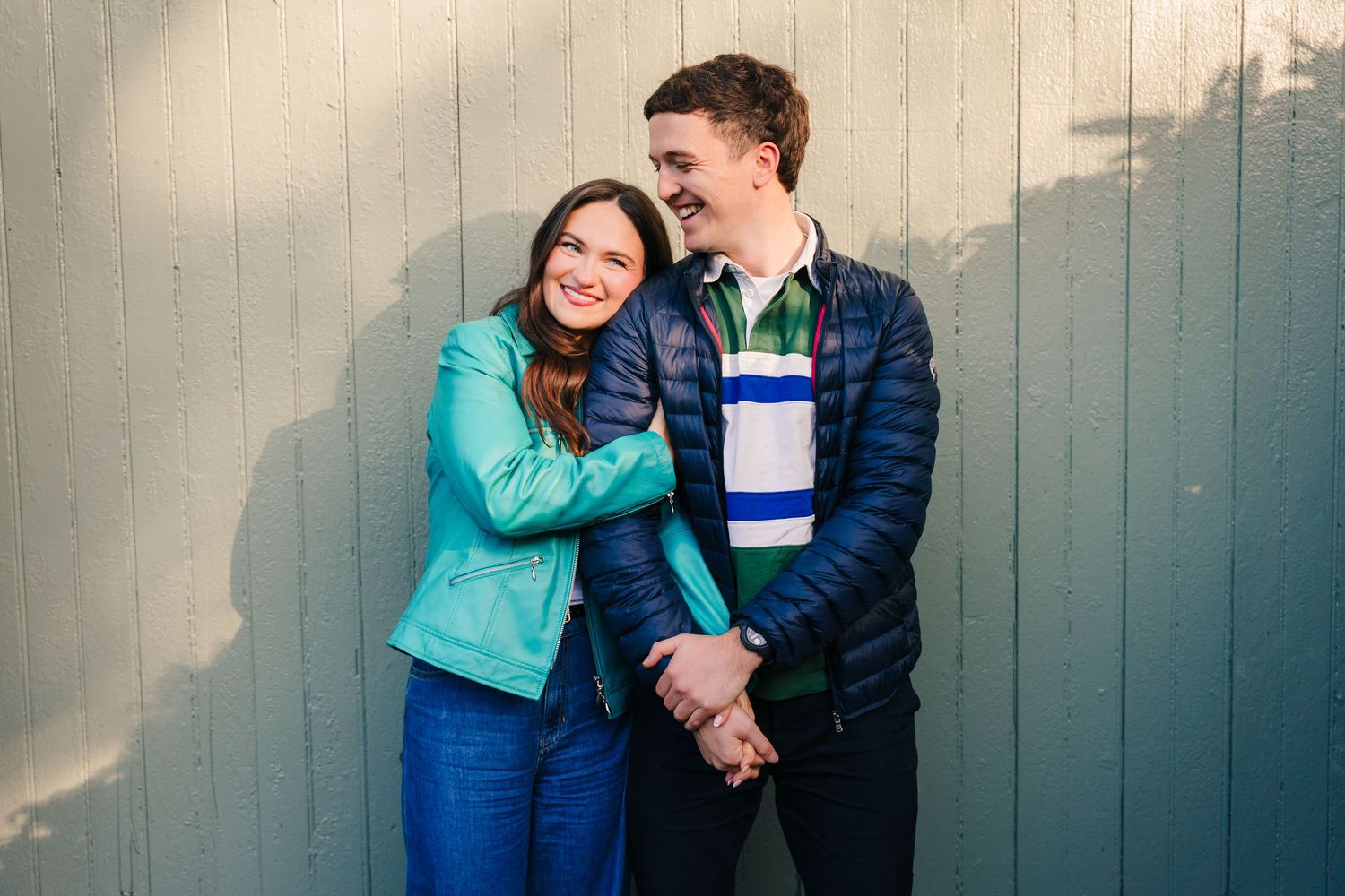 A couple in blue jackets share affectionate moments in a series of candid photos against a gray wall. PHOTOGRAPHER Dublin