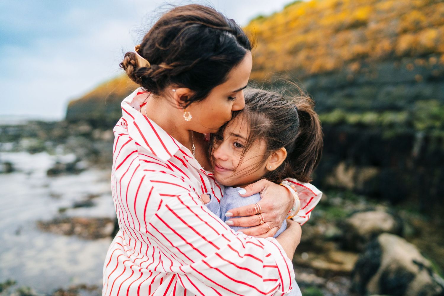 A couple in a red striped shirt sharing tender moments together by a rocky beach during golden hour. family PHOTOGRAPHER Dublin