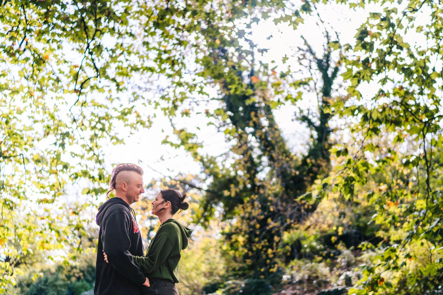 A couple embraces outdoors surrounded by sunlit green foliage. PHOTOGRAPHER Dublin PHOTOGRAPHER Dublin ireland