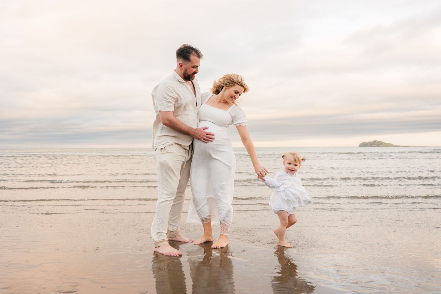 Family walking together on a beach at sunset with reflections in the wet sand. Family PHOTOGRAPHER Dublin