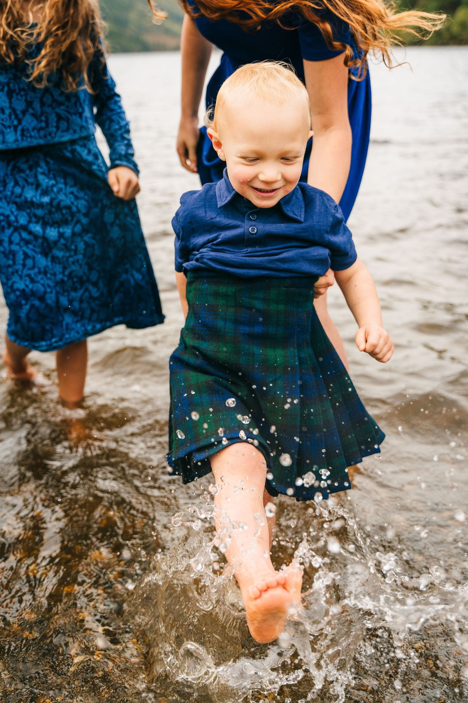 Child in a blue and green outfit splashing and playing in the water at a lake.Family photogrAPHER DUBLIN