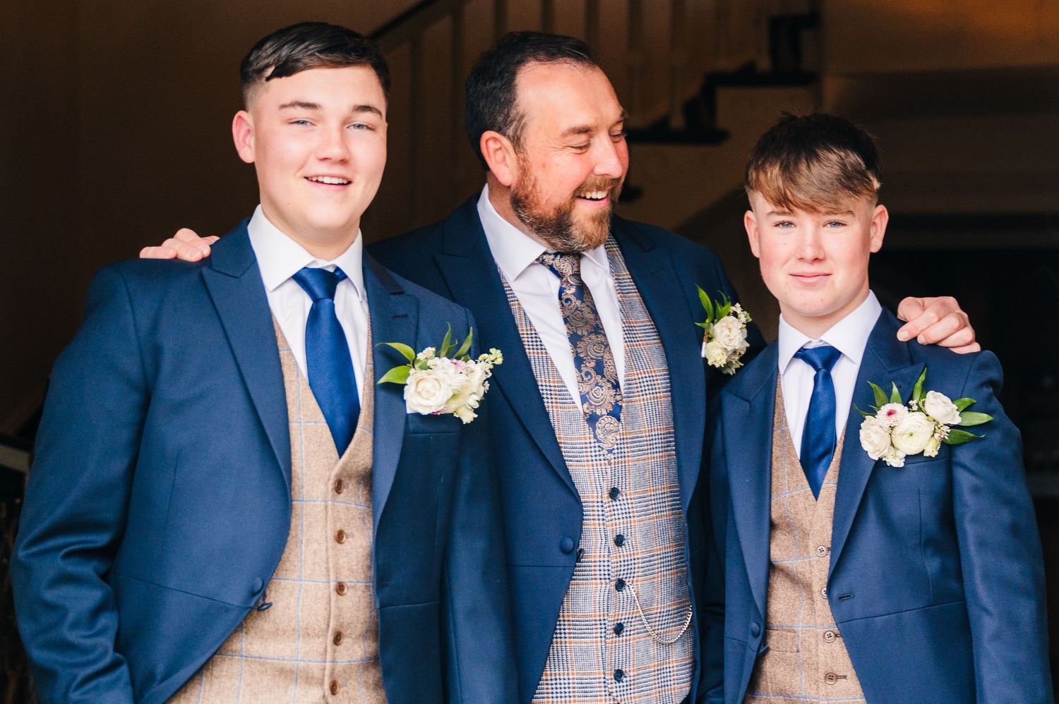 Three people in matching navy blue suits with boutonnières and beige waistcoats stand together at a formal event. Virginia Park Lodge Weddin