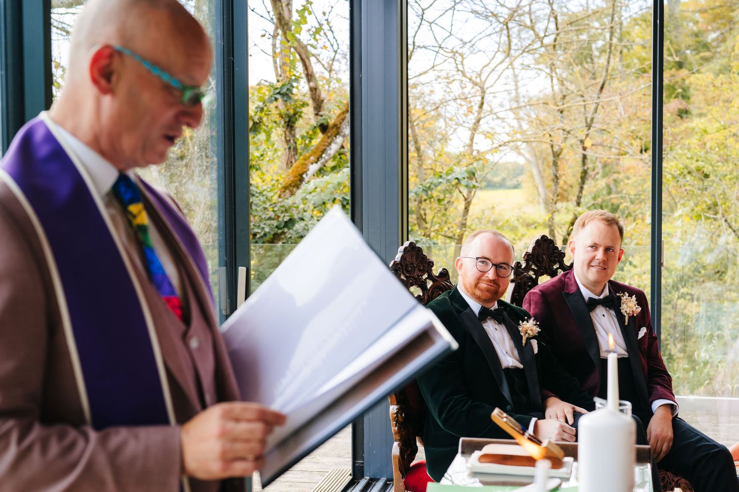 A group of wedding guests stand at a reception venue with drinks and papers in hand. LGBTQ Ashley Park Wedding Photographer