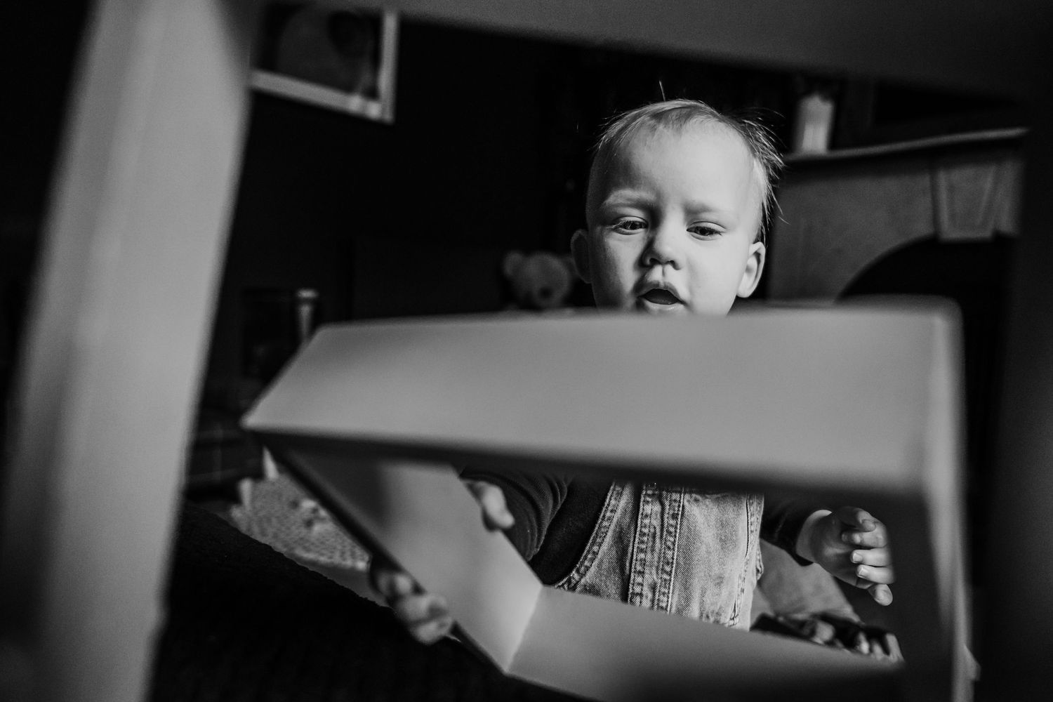 A black and white photo showing a child reading a book through a window or frame.  Family PHOTOGRAPHER Dublin