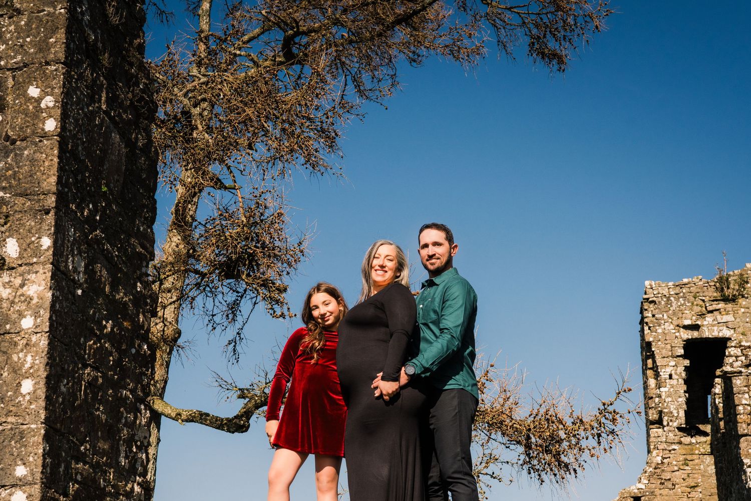 Group poses together between castle ruins on sunny autumn day with blue skies. Family PHOTOGRAPHER Dublin