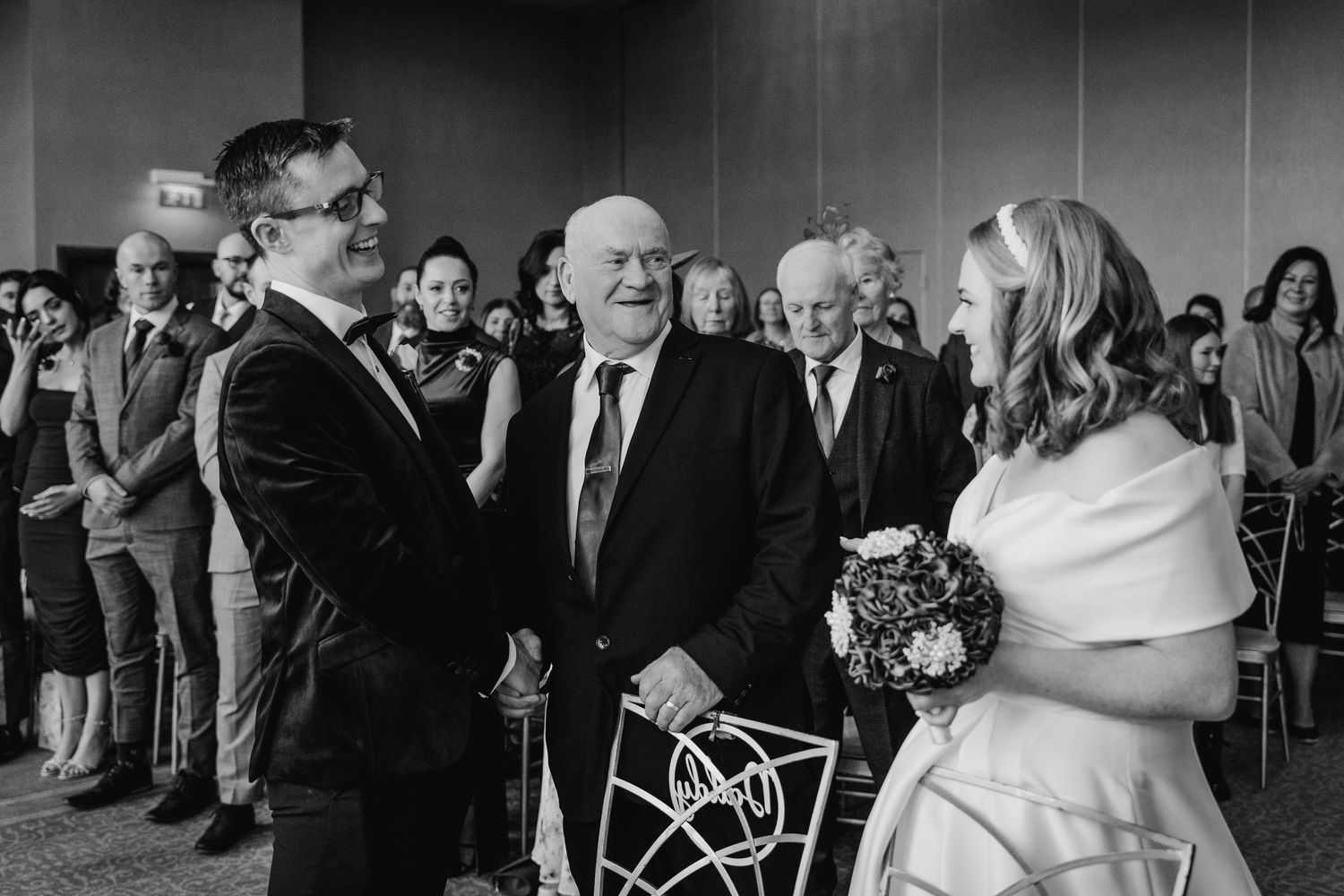 Black and white photo of a wedding ceremony with guests looking on during an emotional moment.  Wedding PHOTOGRAPHER Trim Castle