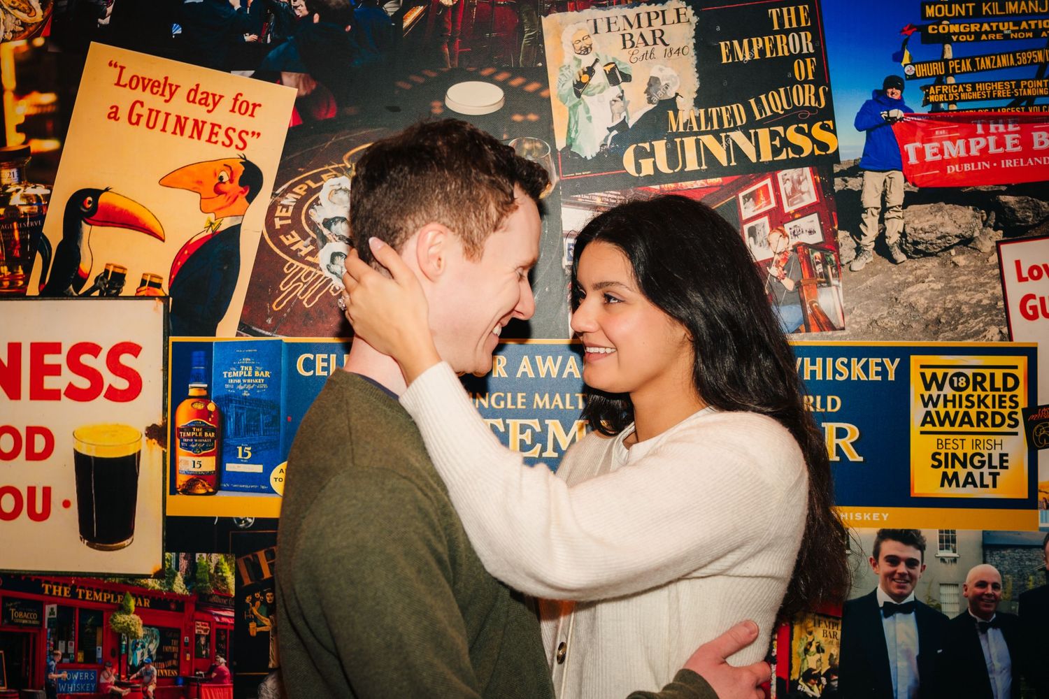 Couple embracing in front of wall covered with vintage posters and advertisements. Surprise proposal dublin photography