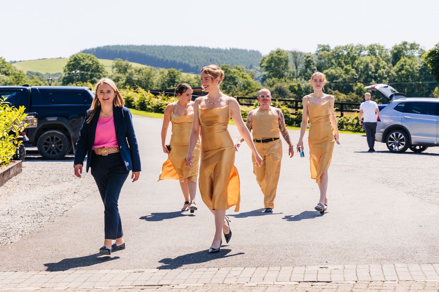 Poulaphouca Wedding photographer wicklow  Wedding party walking down a paved path in yellow dresses with rolling hills in the background.
