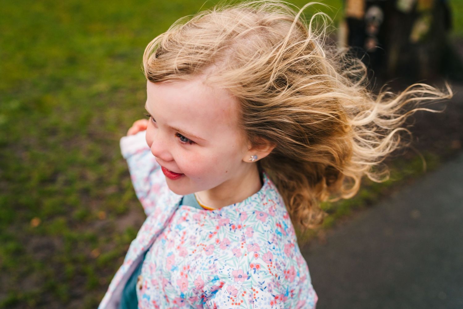 Blonde hair flows in the wind as a joyful child wearing a floral print top smiles during an outdoor moment.Family photographer Dublin Irelan