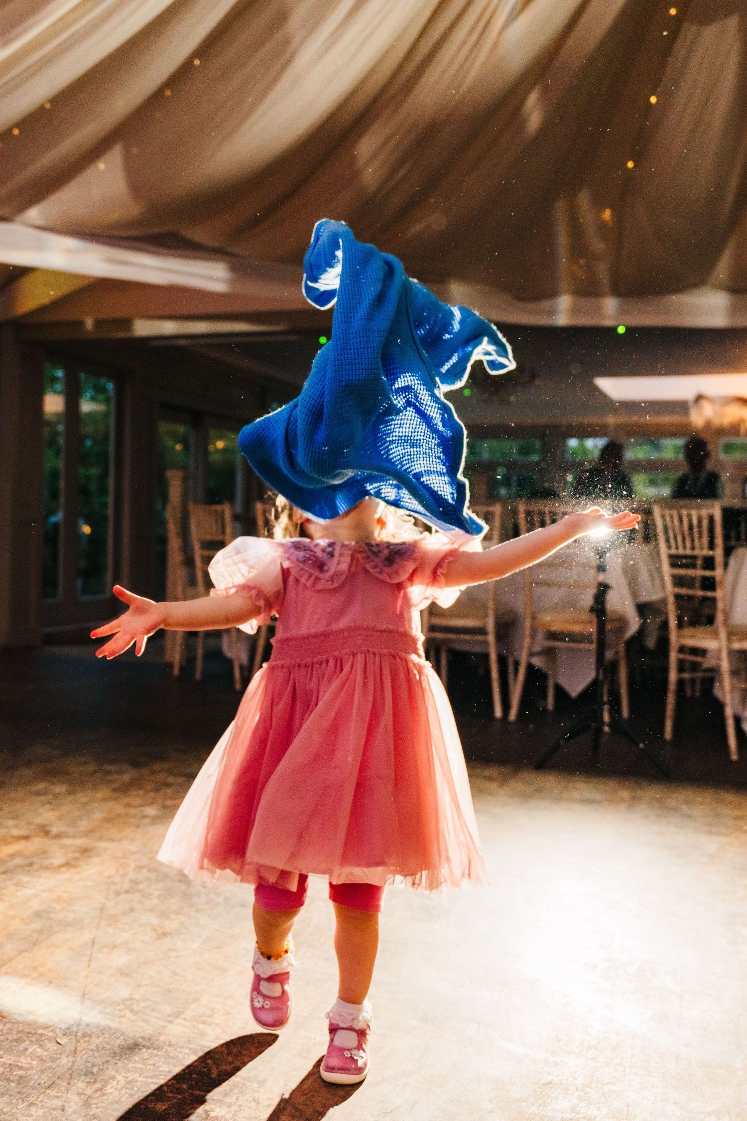 Millhouse slane wedding photographer dublin Young child in pink tulle dress dances under floating blue fabric at wedding reception.