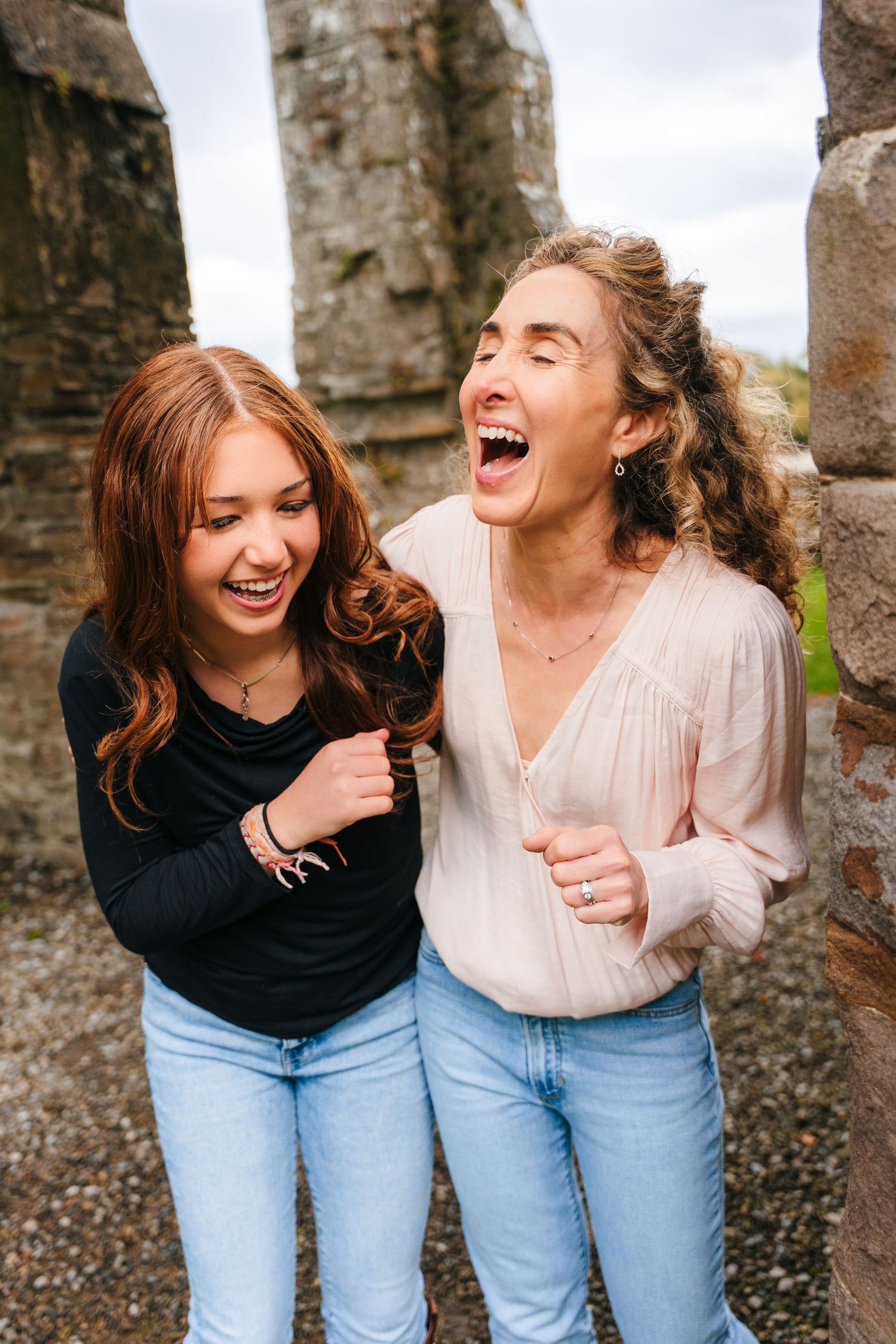 Two friends in jeans share genuine laughter against a stone wall backdrop. BEctive abbey family photographer dublin