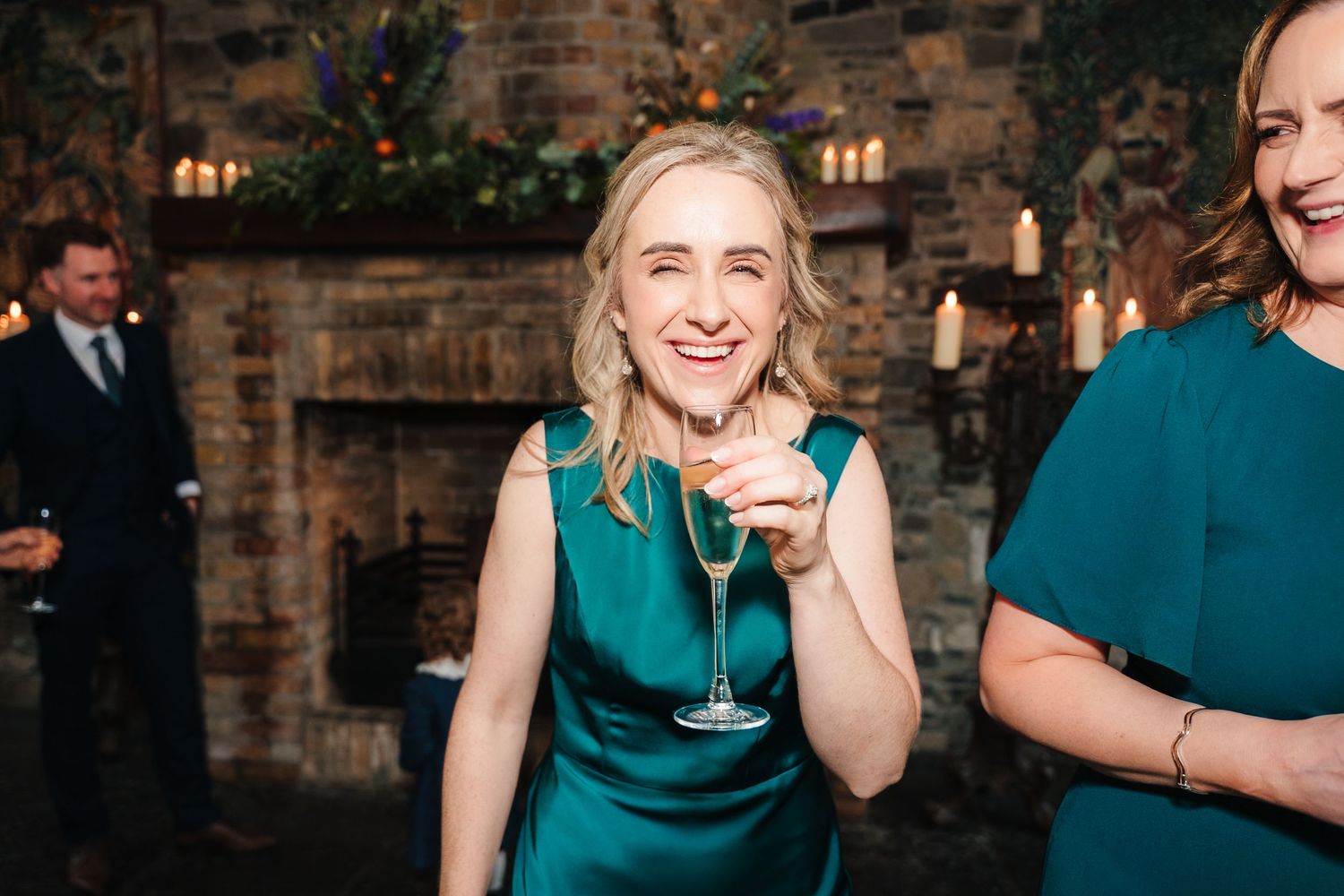 Wedding guests in teal dresses enjoy drinks at an outdoor stone venue.