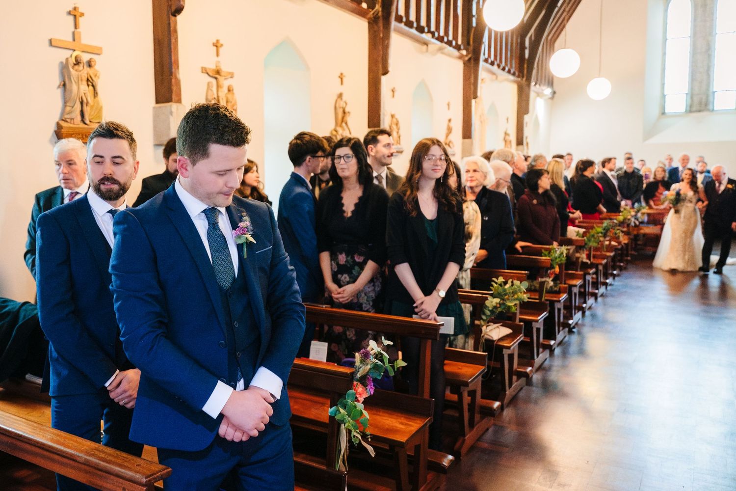 Wedding ceremony in progress inside a church with guests seated in wooden pews.