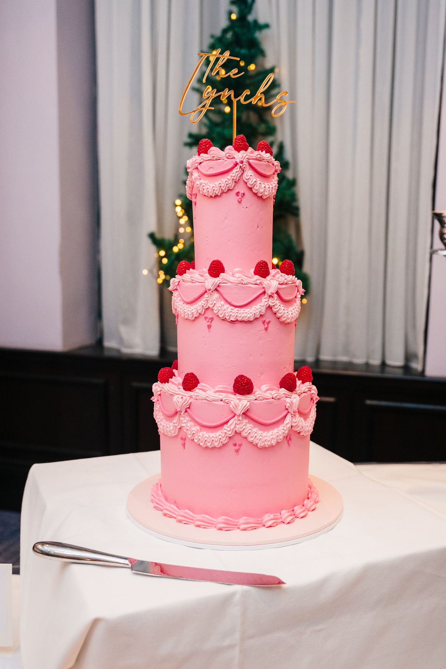 Pink three-tiered wedding cake with scalloped details and red accents displayed on white tablecloth.Wedding photographer dublin