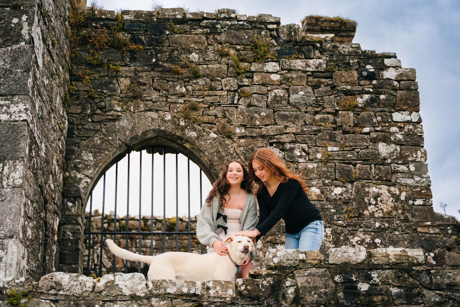 Couple embraces against ancient stone walls and arches of a historic castle ruin on a bright day. BEctive abbey family photographer dublin