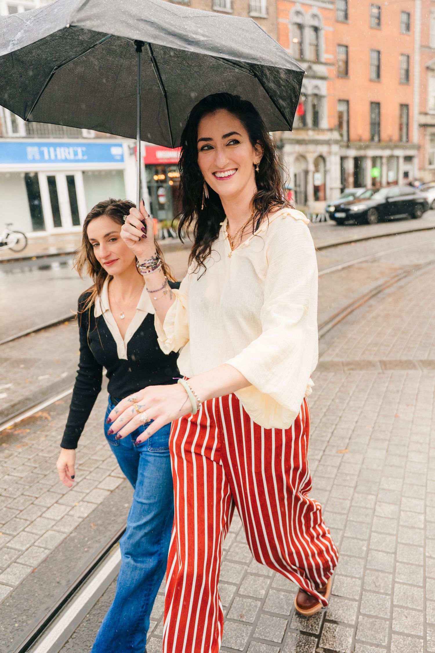 Rainy day fashion shoot on cobblestone street with black umbrellas and casual attire. professional headshots dublin photographer