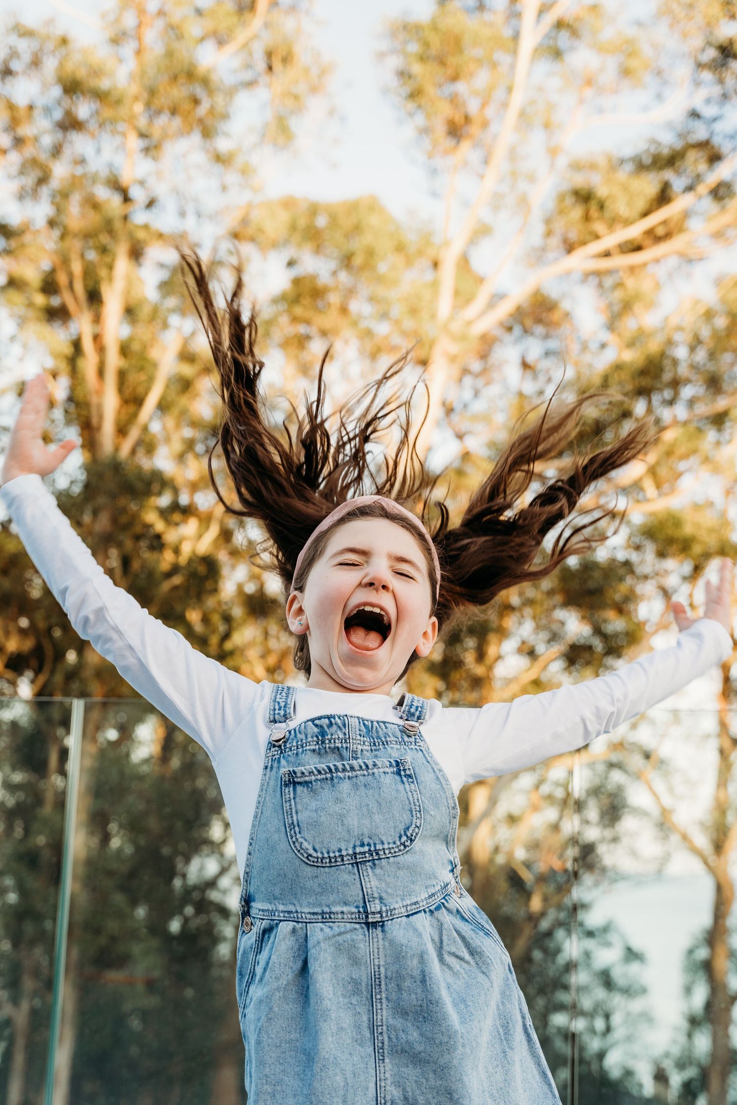 Joyful child in denim overalls jumps with arms raised and hair flying on a sunny autumn day. family PHOTOGRAPHER Dublin