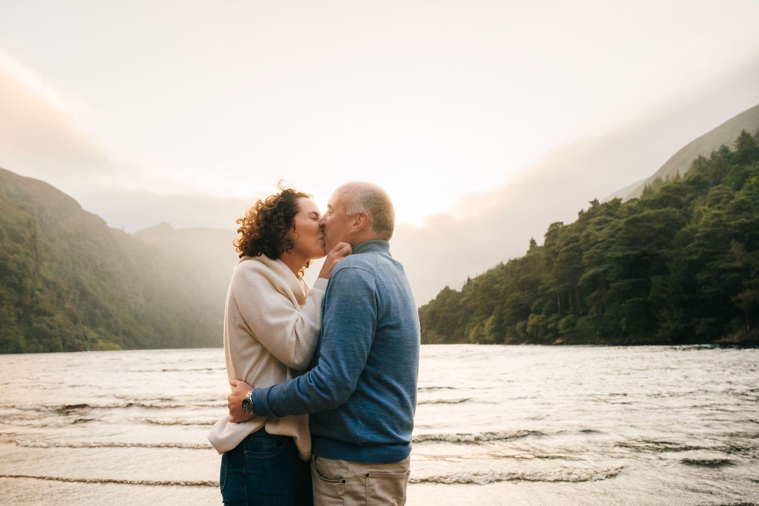 A couple shares a romantic kiss on a scenic beach at sunset with misty mountains in the background. PHOTOGRAPHER Dublin ireland