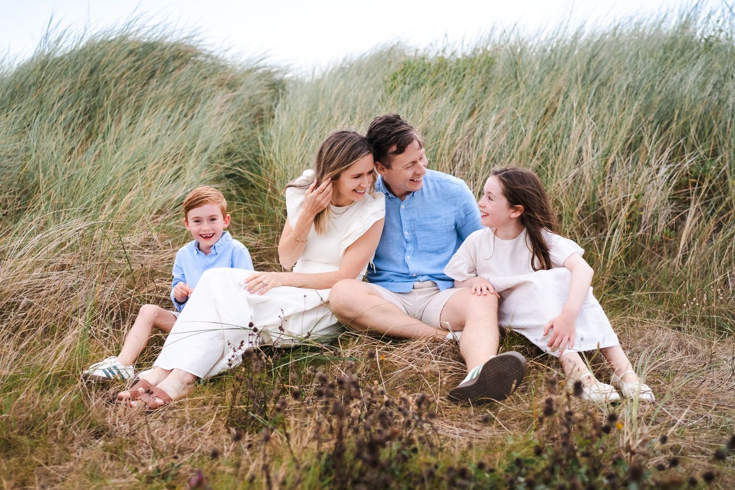 Family relaxing together on grassy dunes near beach grass on a summer afternoon.  Family photographer Dublin Ireland
