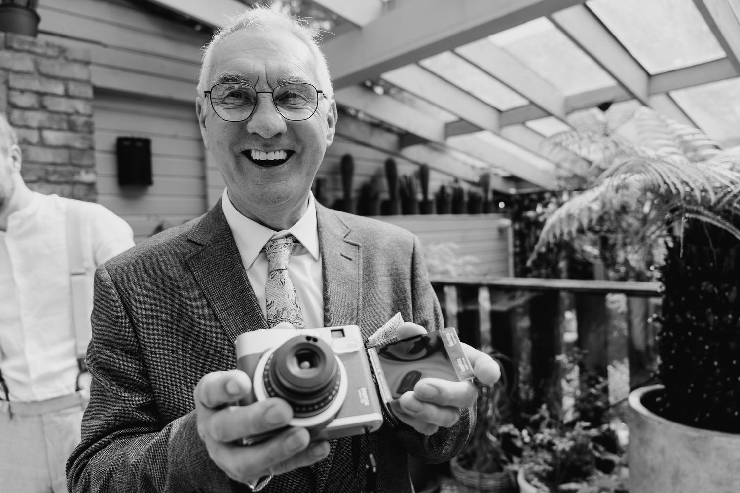 A person in formal attire smiles while holding a vintage camera at an outdoor event. House Dublin Wedding Photographer