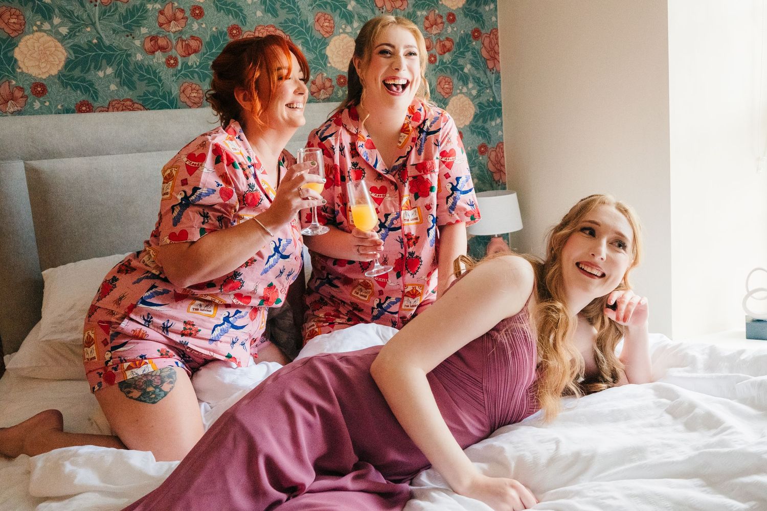 A joyful moment shared between friends wearing matching floral robes during wedding preparations. . Village Barn Tyrrellspass wedding photog