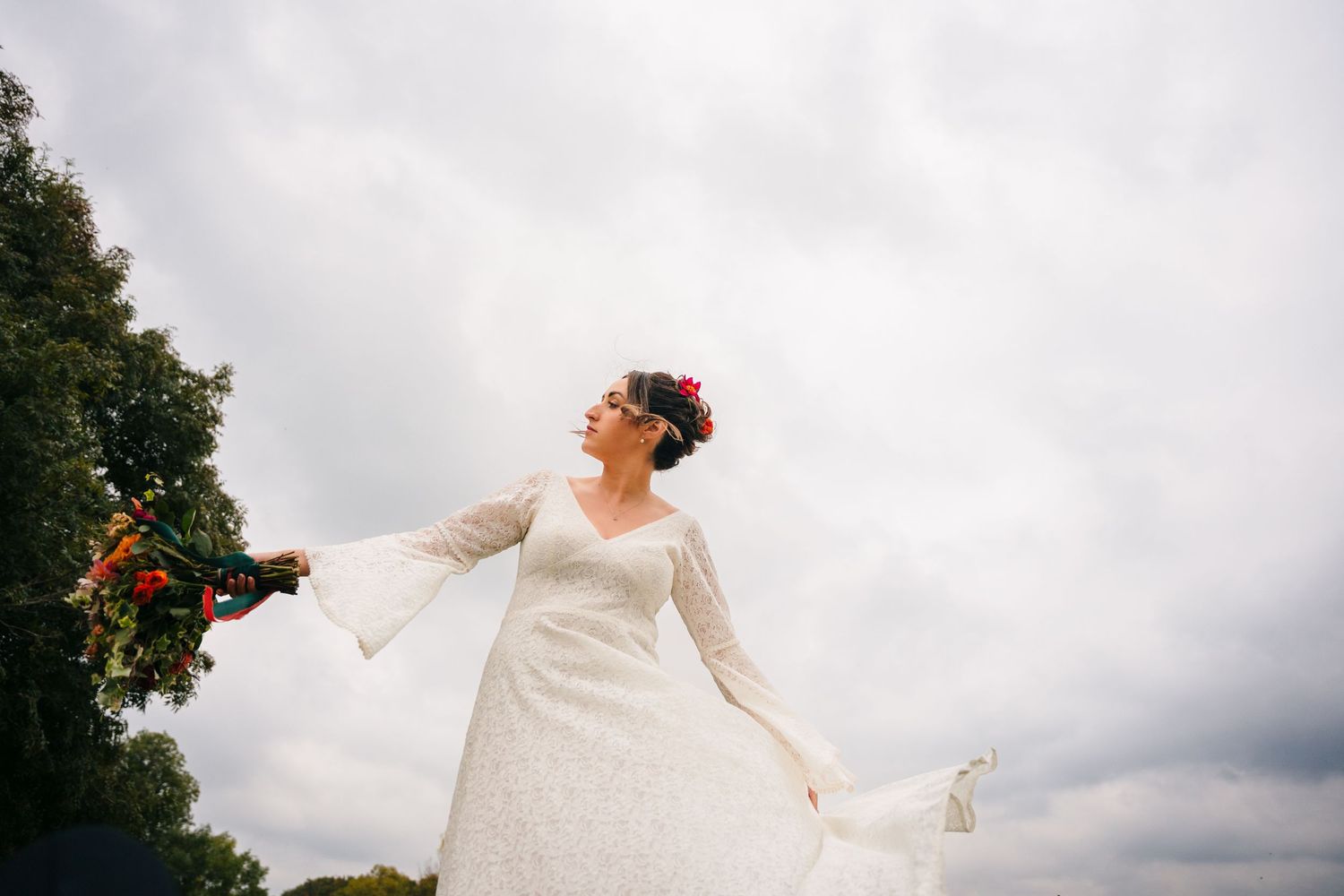 A person in a flowing white dress twirls outdoors against a cloudy sky with trees in the background. Wedding Photography Trim Castle Ireland