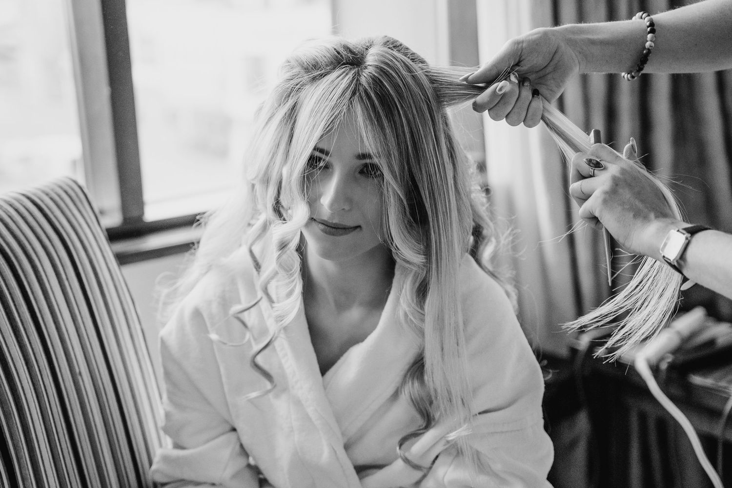 Black and white photo of getting hair styled in a white robe while sitting in a striped chair. Wedding Photography Trim Castle Ireland