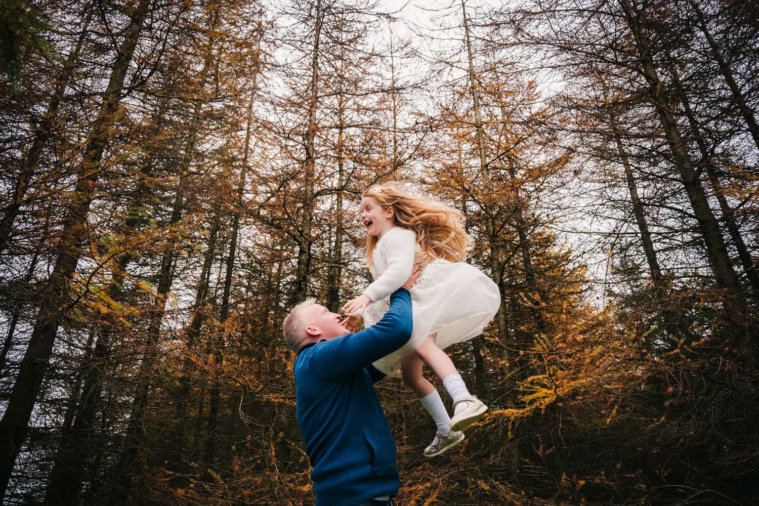 Family Photographer DubA joyful group gathered in a forest with vibrant autumn foliage as the sun peeks through the trees in the background.
