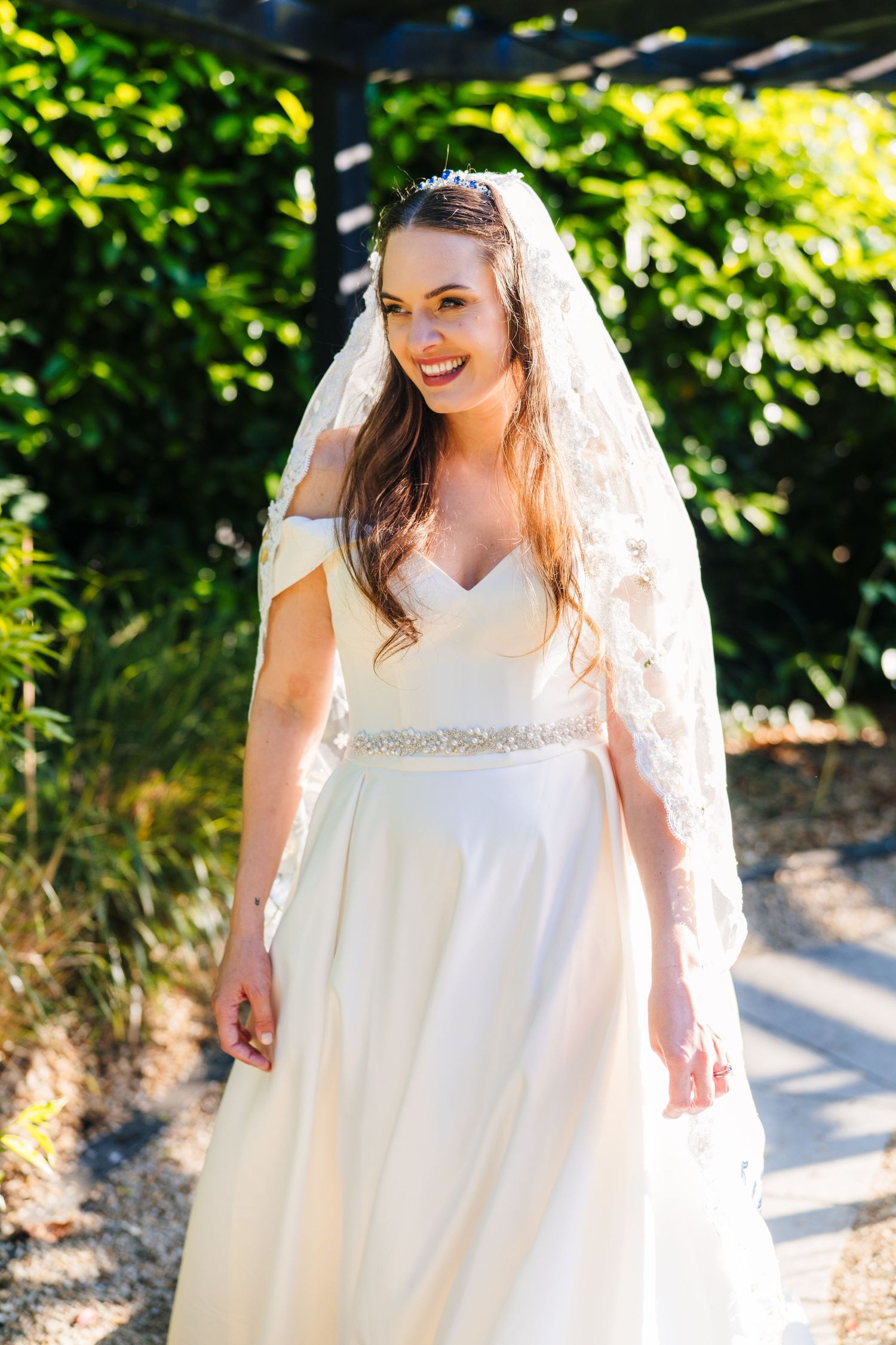 Poulaphouca Wedding photographer wicklow  A radiant bride in a white off-shoulder gown and long veil smiles in natural sunlight.