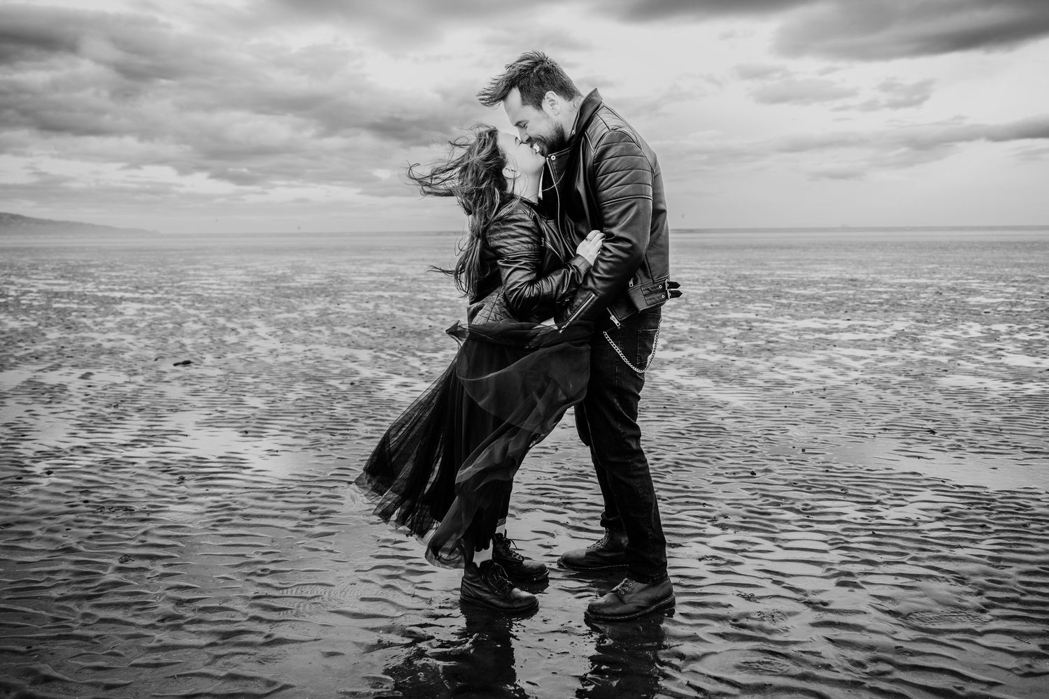 A couple dances along the ocean shore in a dramatic black and white photo sequence at sunset. engagement PHOTOGRAPHER Dublin