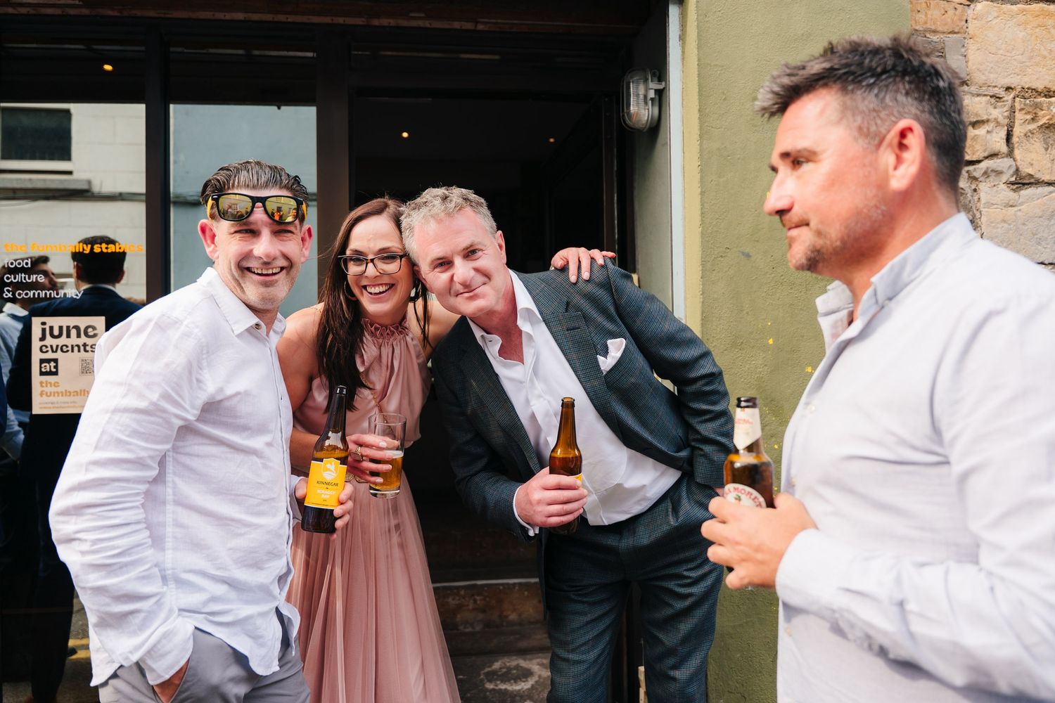 Wedding guests sharing drinks and laughter outside a brick building. Same sex wedding PHOTOGRAPHER Dublin