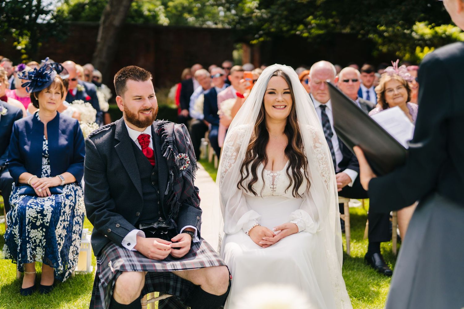 Outdoor wedding ceremony with guests seated on the lawn surrounded by greenery. Portmarnock Hotel Wedding PHOTOGRAPHER Dublin