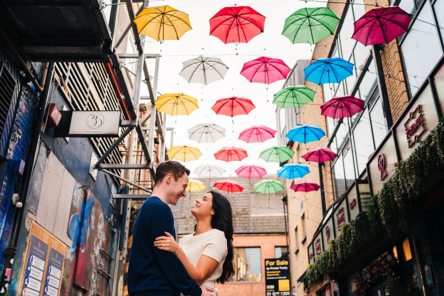 Couple embracing under colorful floating umbrellas in an urban alleyway. Surprise proposal dublin photography