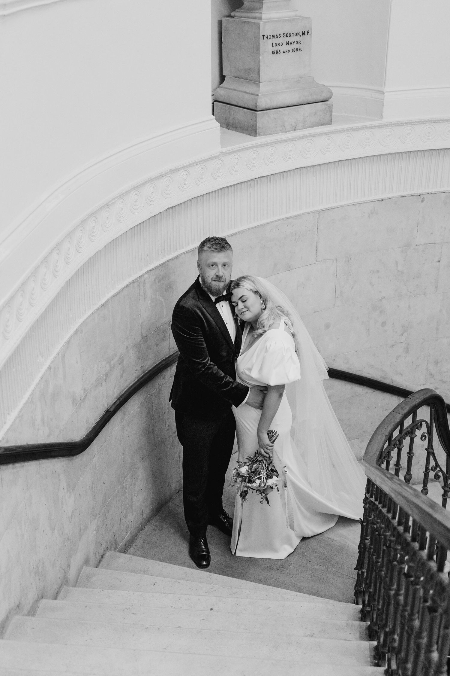 Black and white photos capture newlyweds sharing intimate moments on a grand staircase. City Hall Dublin Photographer