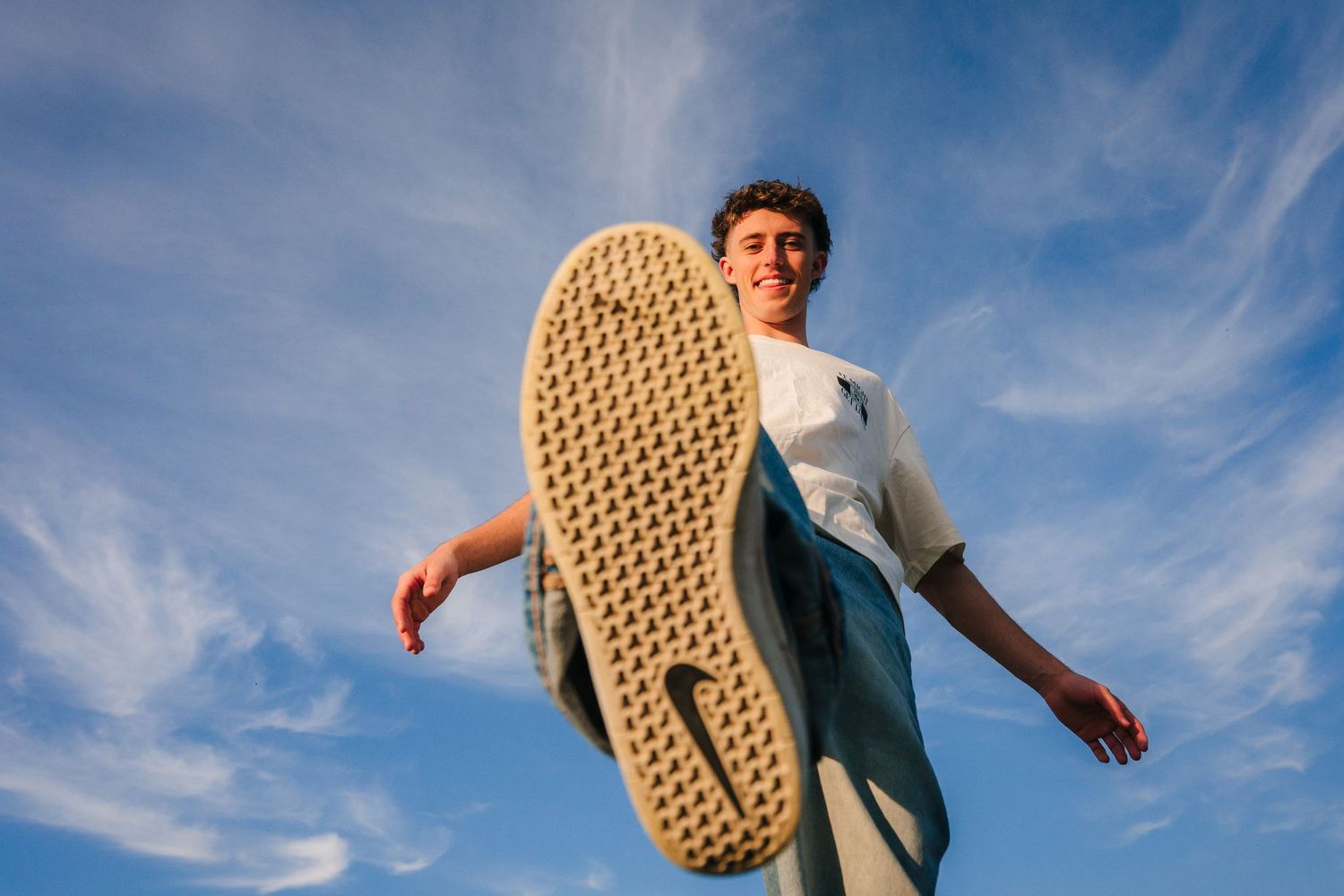 Low angle view of sneakers jumping against a bright blue sky with wispy clouds. Photographer Ireland dublin