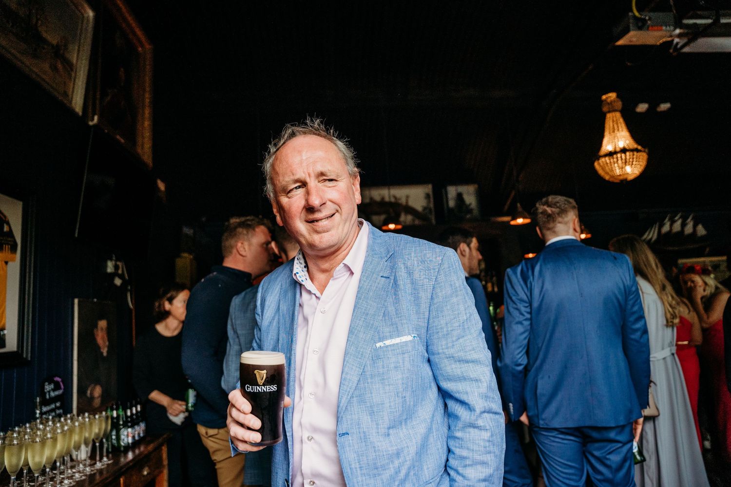 Wedding guest in light blue blazer holds a pint of dark beer at the reception bar. Wedding photographer Dublin