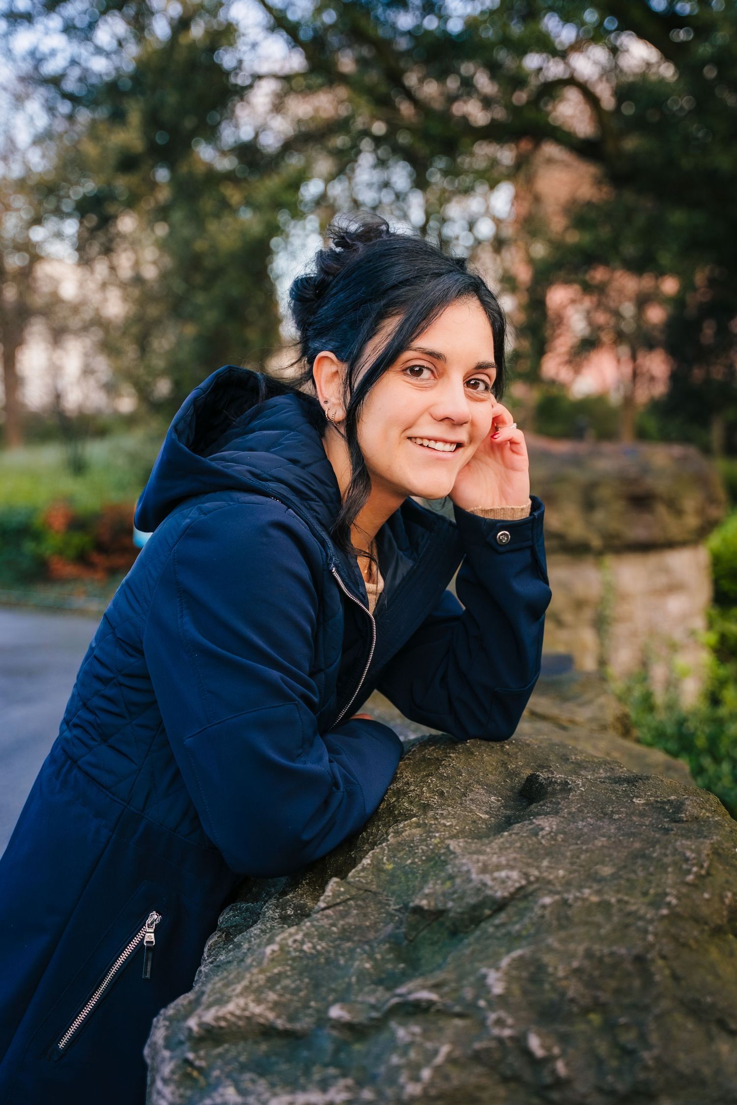 A person in a navy blue hoodie rests their head on a large rock wall while posing outdoors during autumn. professional headshots dublin