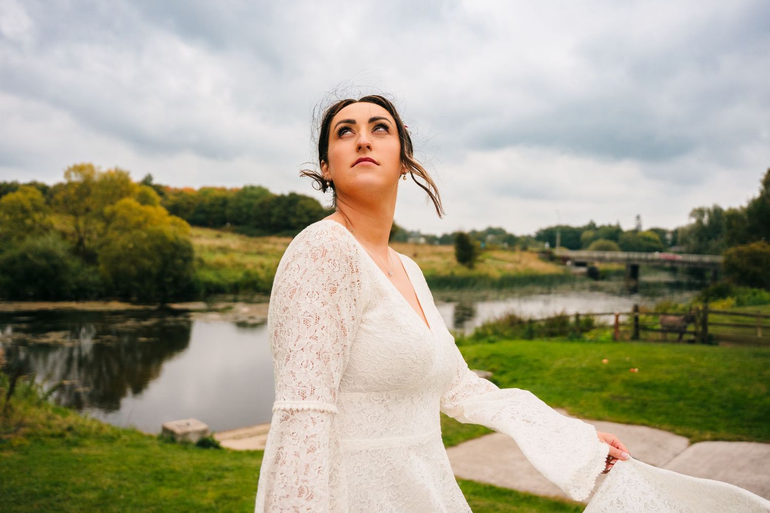 A person in a bell-sleeve wedding dress stands gracefully by a scenic pond.Wedding Photography Trim Castle Ireland