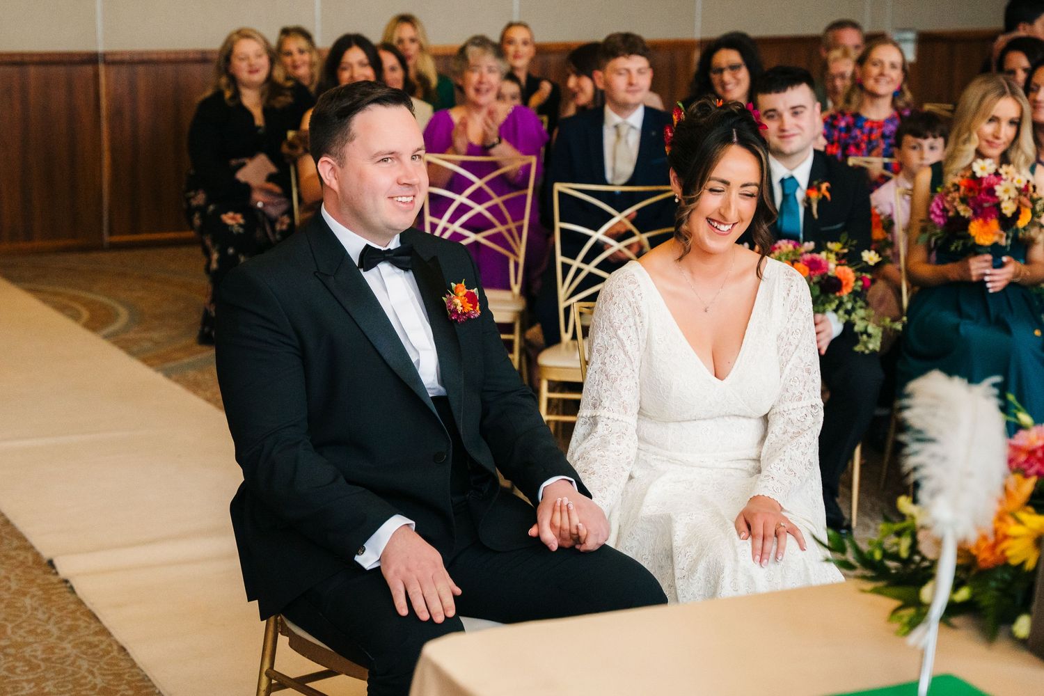 A bride and groom share a joyful moment during their wedding ceremony as guests look on from decorated chairs. Wedding Photography Trim Cast