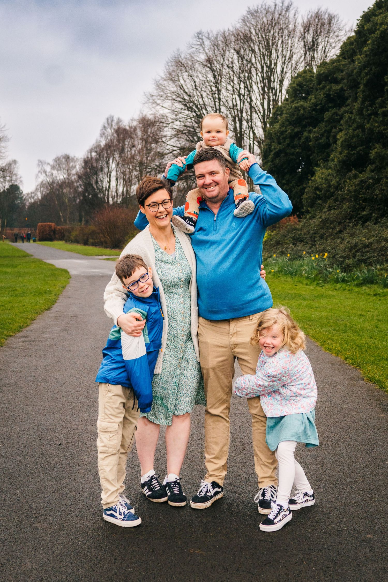 Family photographer Dublin Ireland Family having fun and making silly poses together on a paved trail surrounded by greenery and trees.