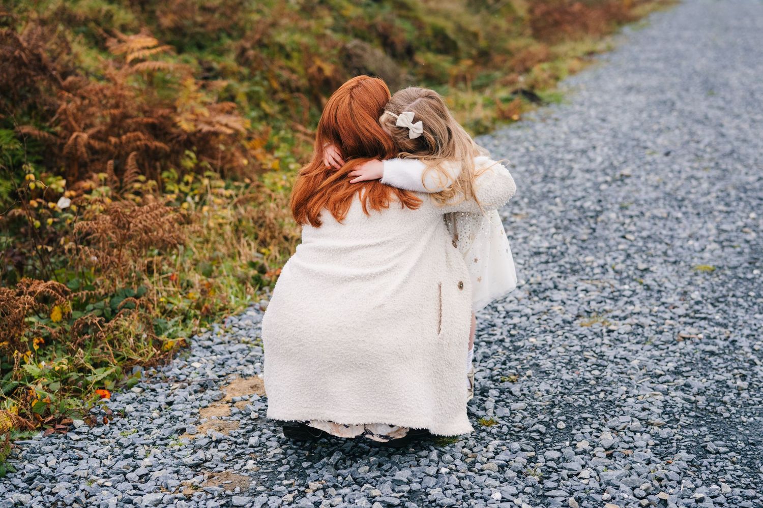 Family Photographer Dublin Ireland  Two people in white dresses share an embrace on a gravel path.